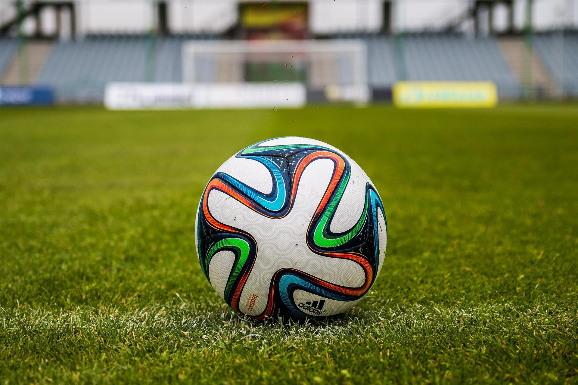A white and patterned football on a grass pitch